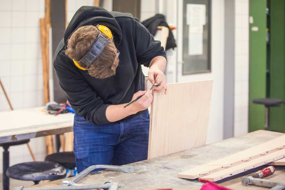 Student zeichnet Markierung auf Holz