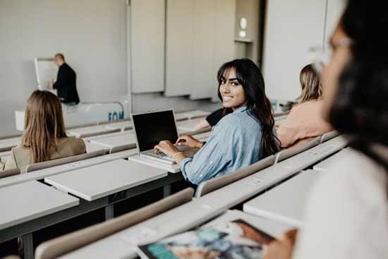 Studentin im Seminar an ihrem Laptop, sie lacht in die Kamera