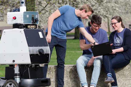 Studis sitzen mit einem Roboter auf dem Campus